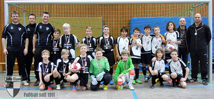 TuRa E2- und E3-Junioren mit Trainern vor Tor in Halle, Spieler tragen schwarze und weiße Trikots, einige mit Medaillen, zwei halten Fußbälle