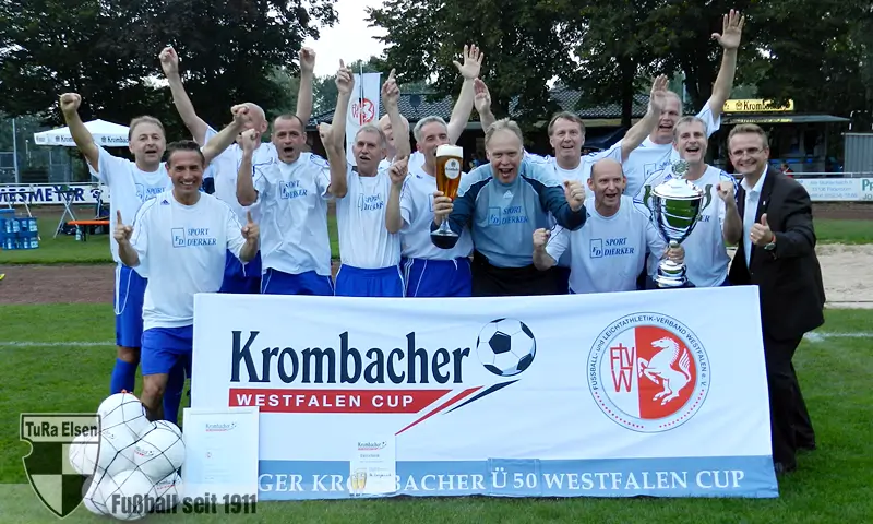 Ü50 Westfalen-Meister Preußen Lengerich Die Mannschaft von Preußen Lengerich in weißen Trikots und blauen Hosen jubelt hinter Banner mit Aufschrift 'Krombacher Westfalen Cup' und hält Pokale