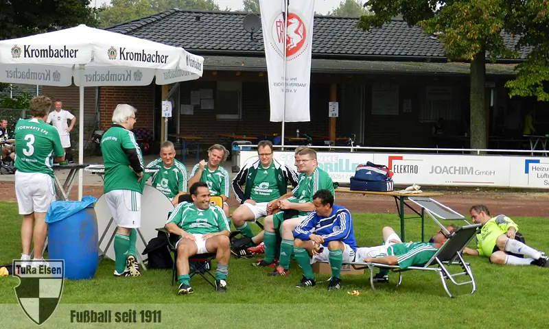 Die Oldies von Vorwärts Epe bei der Regeneration Die Mannschft Vorwärts Epe in grünen Trikots entspannt sich auf der Bank und Liegestühlen neben dem Spielfeld, Banner und Sonnenschirme mit Krombacher-Logo im Hintergrund