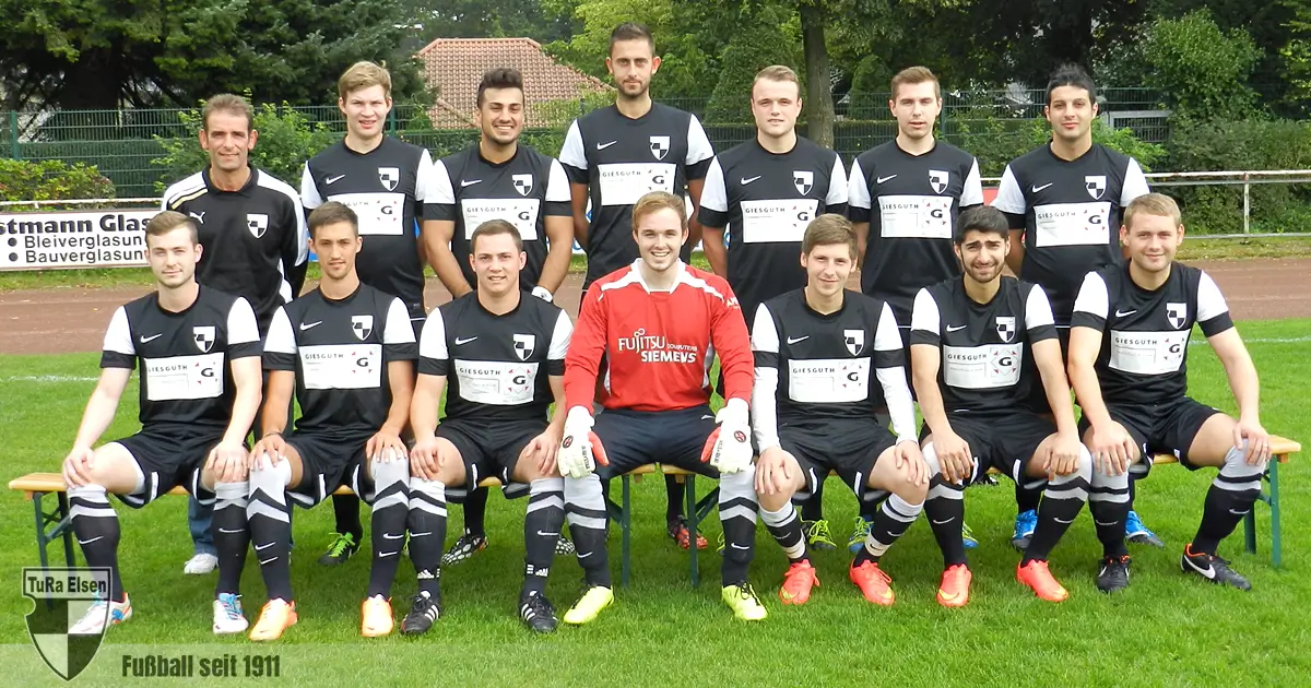 2. Mannschaft der TuRa Elsen, 12 Spieler in schwarz-weißen Trikots, Torwart in rotem Trikot und ein Trainer, sitzend und stehend auf dem Sportplatz