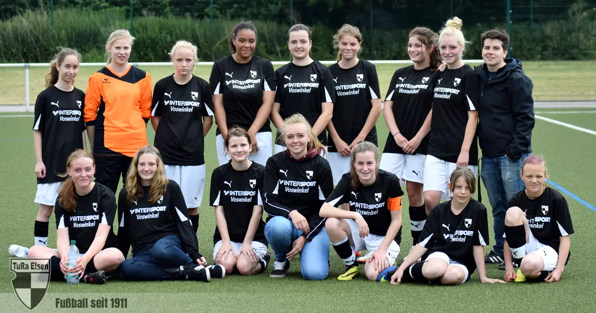 B-Juniorinnen in schwarzen Trikots, posieren auf dem Spielfeld, einige sitzen, andere stehen, die Torfrau trägt ein orangenes Trikot