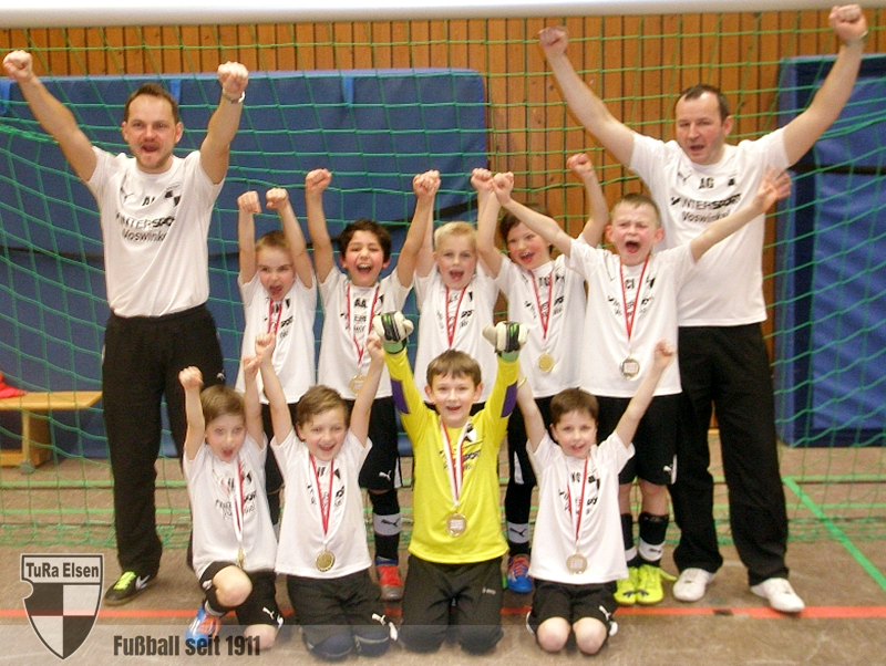 F2-Junioren der TuRa Elsen mit zwei Trainern, alle jubeln mit erhobenen Armen vor einem Hallenfußballtor, Kinder tragen Medaillen