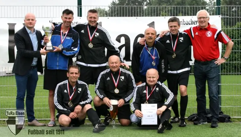 TuRa Altherren Ü50 Fußballmannschaft Ü50 Altherren mit Medaillen und Pokal auf dem Spielfeld, zwei Männer in Anzügen stehen seitlich