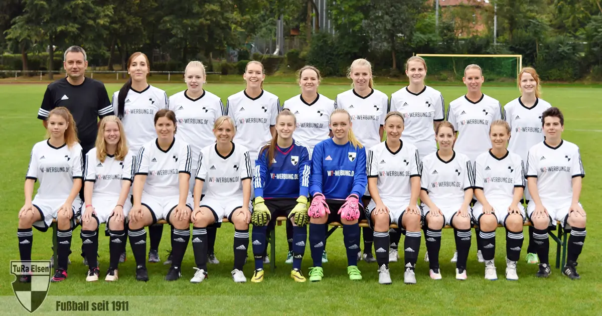 Frauen-Fußballmannschaft TuRa Elsen 2016/17 in weißen Trikots, sitzend und stehend auf dem Spielfeld