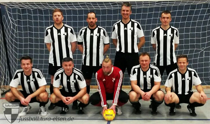Ü40-Fußballer der TuRa Elsen in schwarz-weißen Trikots vor einem Hallenfußballtor, der Torwart in rotem Trikot hält einen gelben Ball