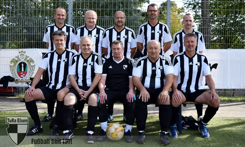 Ü50 TuRa Elsen in schwarz-weißen gestreiften Trikots posieren in zwei Reihen, ein Fußball liegt vor ihnen