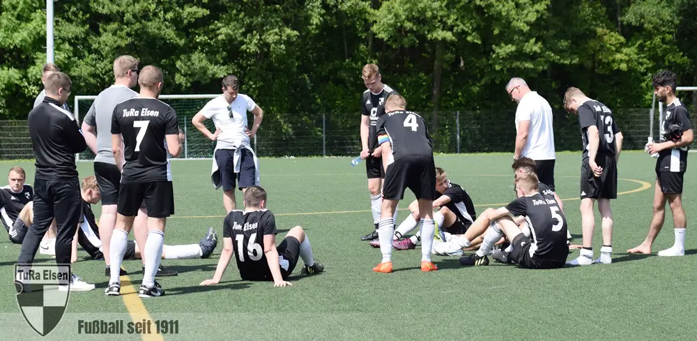 Schockstarre bei den TuRa Spielern nach der 6:4 Niederlage am letzten Spieltag bei Suryoye Paderborn und dem damit verbundenen Abstieg  Spieler der 1. Herrenmannschaft der TuRa Elsen in schwarzen Trikots versammelt auf dem Spielfeld, einige Spieler sitzen enttäuscht auf dem Boden, nach Niederlage und Abstieg