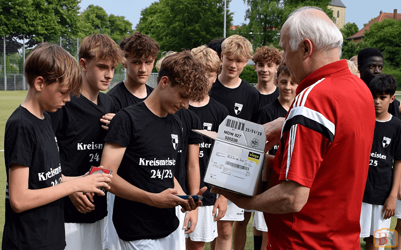 Die stolzen TuRa-Kicker erhalten die Kreismeister-Medaille vom Staffelleiter TuRa-Spieler in schwarzen Trikots erhalten Medaillen vom Staffelleiter in rotem Shirt auf einem Fußballfeld