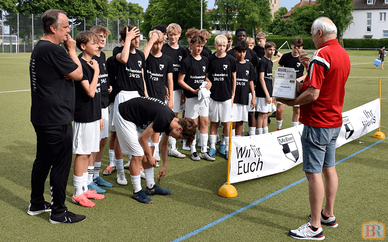 Staffelleiter Holger Beckmann lobt die TuRa Kicker für die herausragende Saison Der Staffelleiter in rotem Shirt ehrt die TuRa-Spieler in schwarzen Trikots auf dem Spielfeld