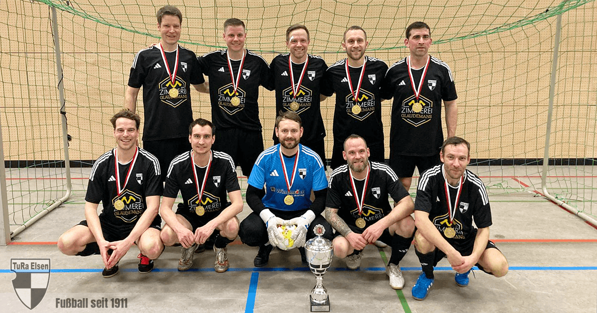 Zehn TuRa-Spieler in schwarzen Trikots mit Medaillen und Pokal posieren in einer Halle vor einem Tor.
