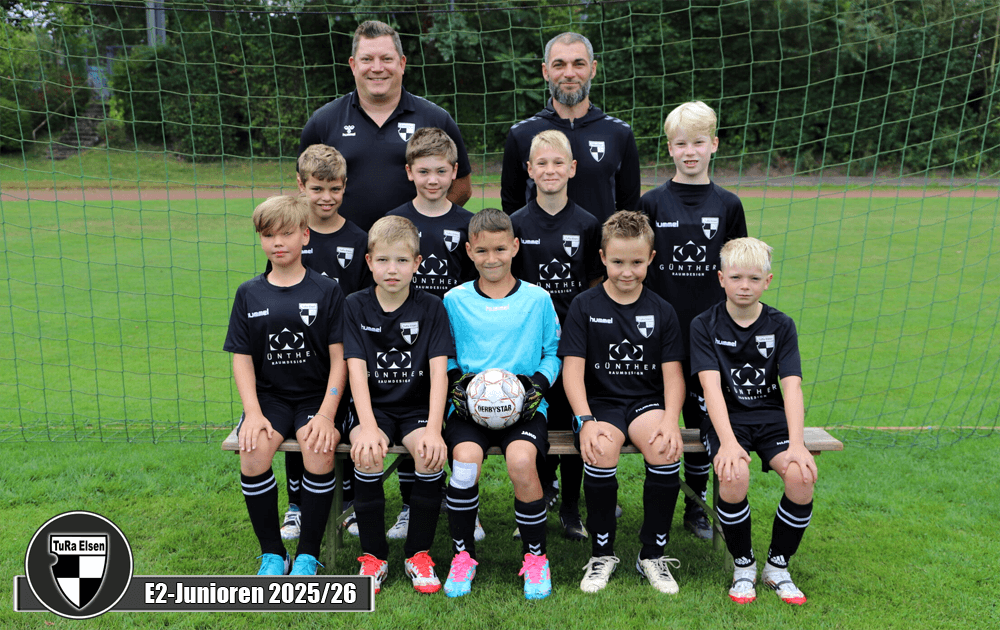 Neun Kinder in schwarzen Fußballtrikots stehen und sitzen vor einem Fußballtor. Zwei Trainer steht hinter ihnen.