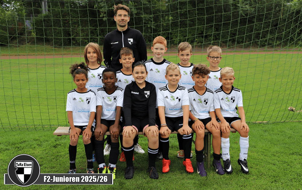 Mannschaftsfoto der F2-Junioren der TuRa Elsen für die Saison 2025/26. 10 Spieler*innen in schwarzen Trikots und eine Torfrau in Schwarz, ein Trainer im Hintergrund.